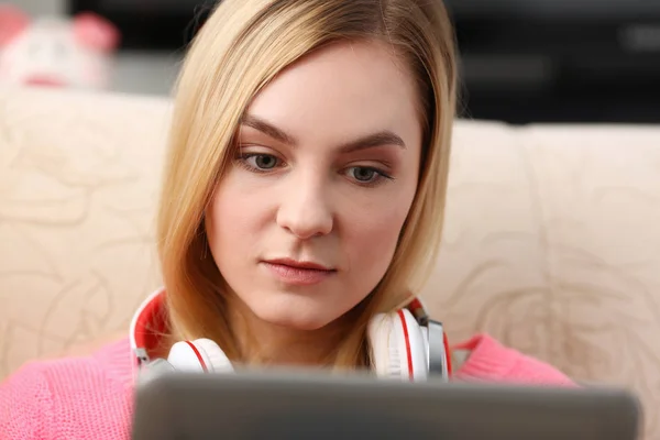 Young beautiful blond woman sit on the sofa in livingroom hold tablet in arms listen to music — Stock Photo, Image