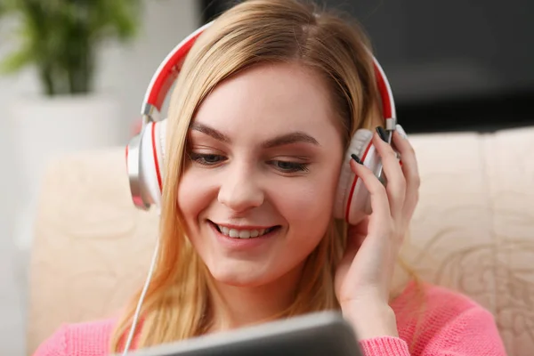 young beautiful blond woman sit on the sofa in livingroom hold tablet in arms listen to music