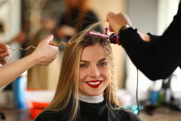 Руки парикмахера держат щипцы для завивки и делают
