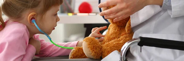 Küçük kız silah oyuncak stetoskop oyuncak ayı ile oynarken tutun — Stok fotoğraf