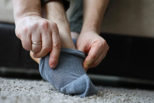 Homem em casa de manhã coloca meias cinza em sua perna — Fotografia de Stock