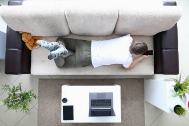 Adam kanepeye uzanıp modern akıllı telefonu elinde tutuyor.