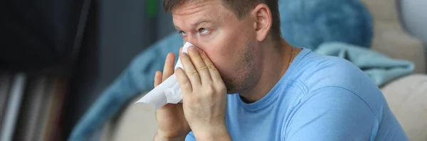Man blowing his nose in a napkin while sitting — Stock Photo, Image