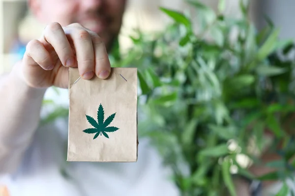 Man hand hålla papper paket med marijuana symbol närbild bakgrund — Stockfoto