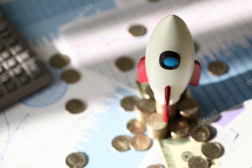 Toy space rocket stands on coins near calculator