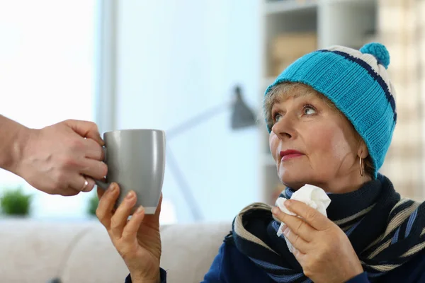 Cold elderly lady in knitted hat takes cup tea — Stock Photo, Image