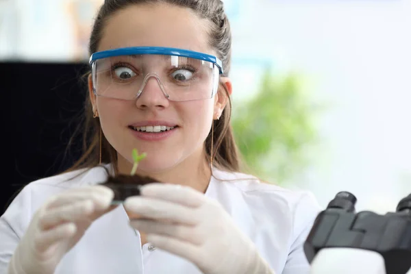 Girl laboratory assistant admires sprout earth — Stock Photo, Image
