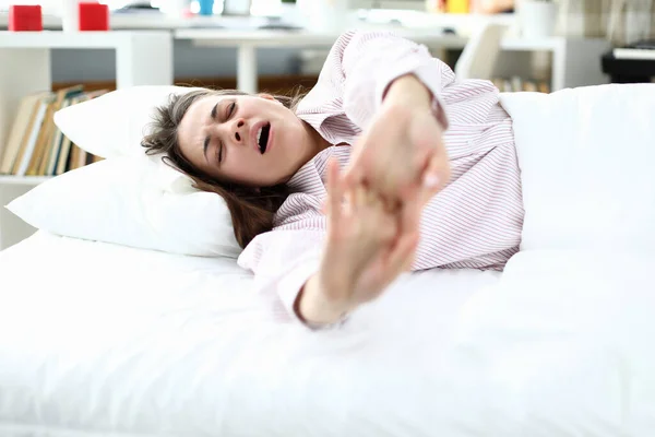 Girl in pajamas lies on bed and stretches, yawning — Stock Photo, Image