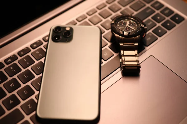 Silver smartphone and watch lie on laptop keyboard in office close-up