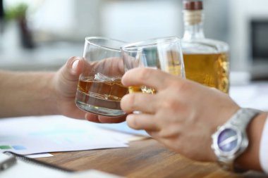 Men sit workplace and drink alcohol from glasses