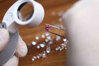 Jeweler examines red gem under magnifying glass