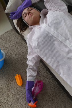 Girl in gloves for cleaning lies sofa from fatigue