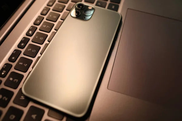 Серебряный смартфон лежит на клавиатуре ноутбука в офисе крупным планом — стоковое фото
