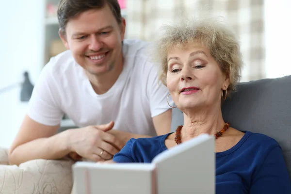 Пожилая леди сидит на диване и смотрит альбом со своим сыном — стоковое фото