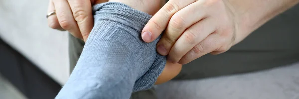 Man at home in morning puts gray socks on his leg