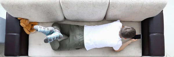Adam kanepeye uzanıp modern akıllı telefonu elinde tutuyor. — Stok fotoğraf