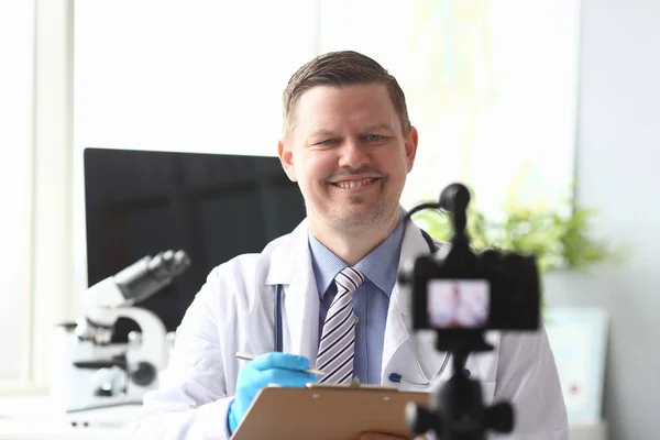 Doctor makes notes in folder in front video camera — Stockfoto