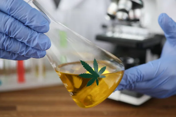 Gloved hands holding glass flask with hemp oil — Stock Photo, Image