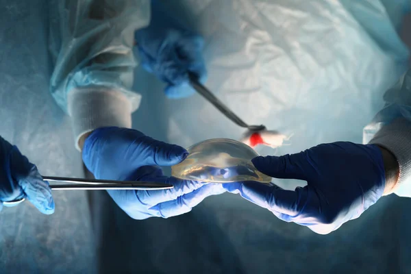 Surgeons holding instruments and breast implant — Stock Photo, Image