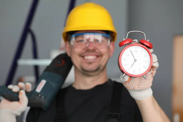 Мужской шлем строителя смеется показывая будильник — стоковое фото
