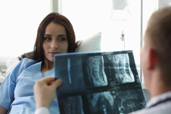 Patient liegt auf Bett und schaut Arzt mit Röntgenbild an — Stockfoto