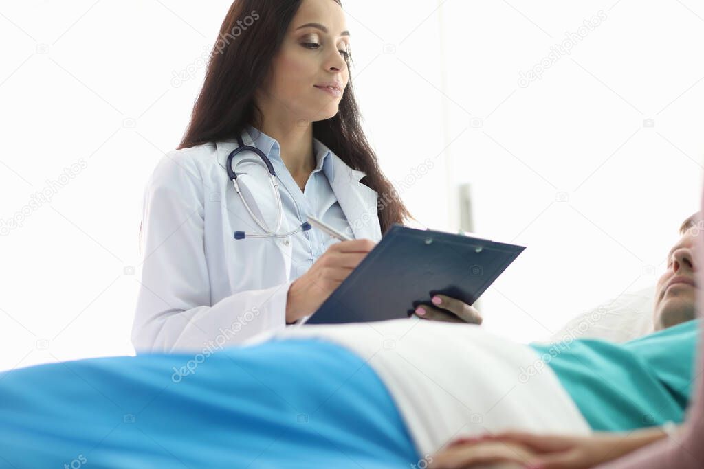 Female doctor stands over man lying hospital bed