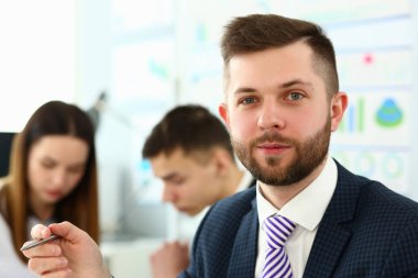 Takım elbiseli ve kravatlı genç tezgahtar kameraya bakıyor.