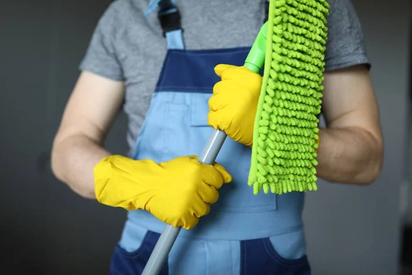 Man in work clothes, cleaning agent, holds mop