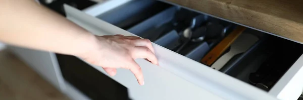 Female hand opens kitchen drawer with cutlery