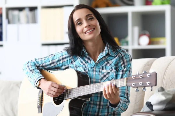 Mulher sentada em casa no sofá e tocando guitarra — Fotografia de Stock