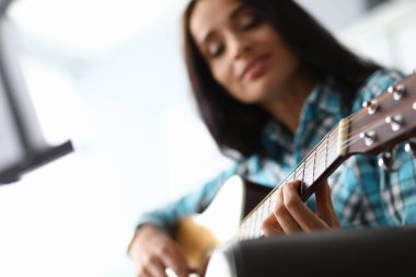 Genç bir kadın evdeki kanepede gitar akorları çalıyor.