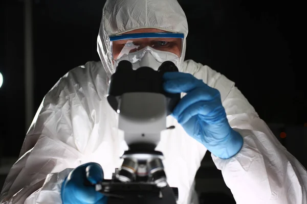 Man in protective suit looks through microscope — Stock Photo, Image