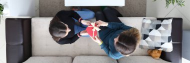 Two lesbian woman sit at sofa and present gift closeup top view