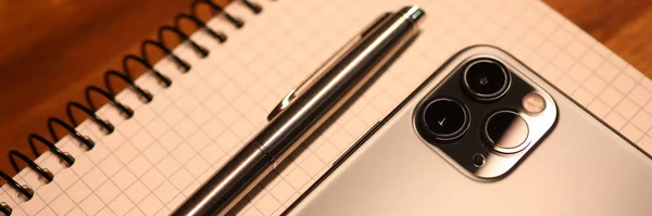 Smartphone argenté et ordinateur portable avec stylo se trouvent sur une table en bois dans le bureau close-up — Photo