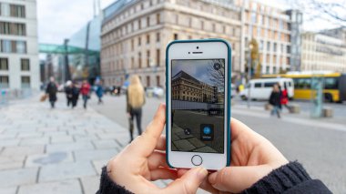 Berlin, Almanya - 8 Kasım 2019: Turist mobil uygulama kullanıyor ve Berlin Duvarı 'ndaki kamera ve tarihine bakıyor. Duvar 'ın bir kısmı Reichstag binası yakınlarında gösteriliyor.. 