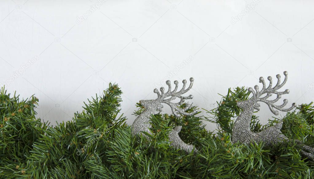 Christmas background, green garland, silver fawn on a white background.