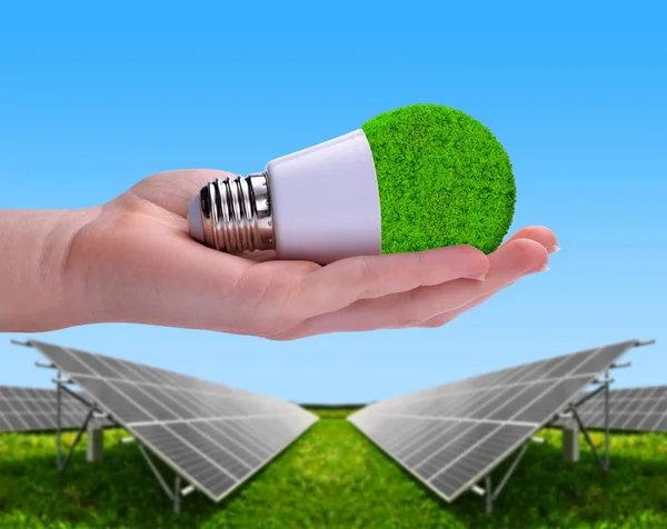 Eco Led lampa i handen i bakgrunden solenergi paneler. — Stockfoto