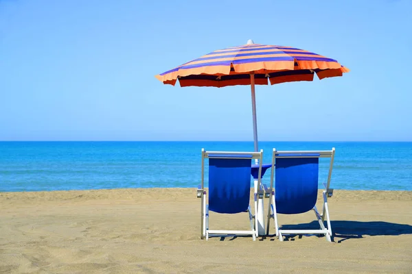 Paar ligstoelen en parasol parasol op het strand. — Stockfoto