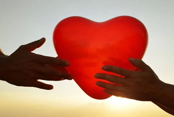 Silueta de manos sosteniendo globo rojo en forma de corazón . — Foto de Stock