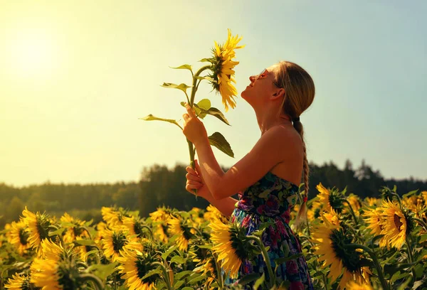 Hermosa chica en el campo oliendo un girasol . —  Fotos de Stock