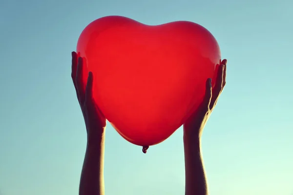 Manos sosteniendo globo rojo en forma de corazón . — Foto de Stock