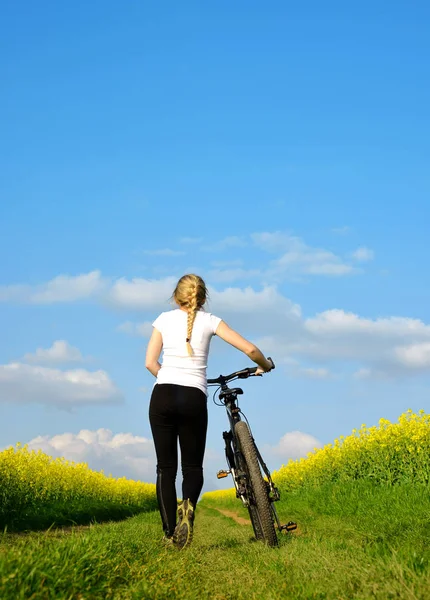 菜の花畑のダート道に自転車を持つ少女 健康的なライフ スタイルのコンセプト — ストック写真