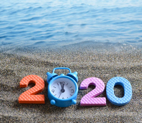 Number 2020 and alarm clock on the sand beach. Happy New Year and  summer holiday concept.