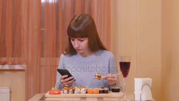 Hezká dívka jí sushi a drží telefon — Stock video