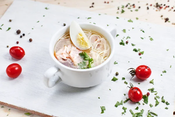 Sup dengan daging ayam, mie dan telur pada memotong papan putih di atas meja kayu dengan tomat ceri dan sayuran — Stok Foto