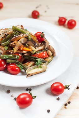 kiraz domates ve yeşillik ile ahşap bir masa üzerinde bir kesme tahtası üzerinde beyaz bir plaka üzerinde ızgara sebze