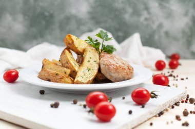 yeşillikleri ile beyaz bir plaka üzerinde bir pirzola ve ahşap bir masa üzerinde bir beyaz kesme tahtası üzerinde kiraz domates ile baharat ile kızarmış patates