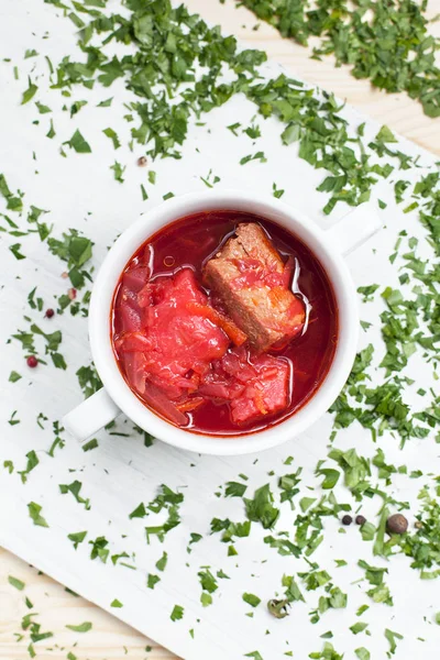 Beet soup with vegetables, herbs and meat in a white bowl on a cutting board on a wooden table — Stock Photo, Image