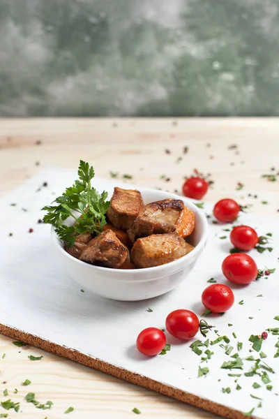 Hidangan daging dalam mangkuk putih dengan sayuran dan tomat ceri di atas papan potong putih di atas meja kayu — Stok Foto
