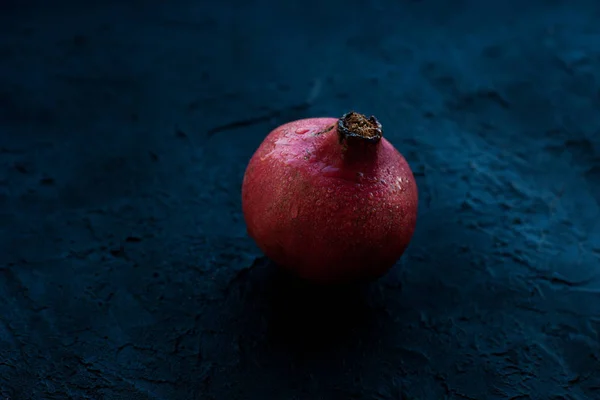 Ett granatäpple på en Mörkblå bakgrund i droppar vatten — Stockfoto